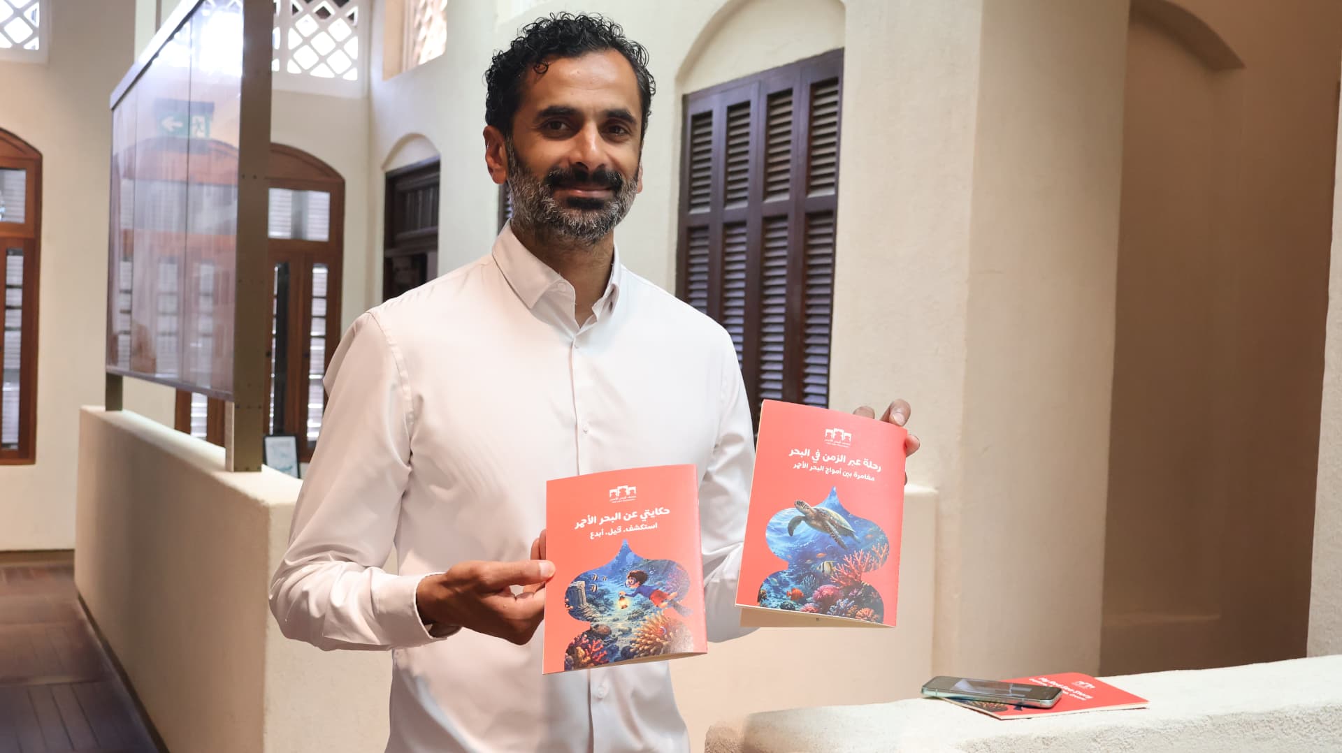 Arabic and English editions of the My Red Sea Story book held up outside the museum